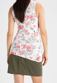 Top sin mangas floral en blanco con flores rosas y verdes; combinado con una falda verde oscura con un dobladillo asimétrico.