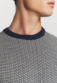 Tmavě modrý a krémový svetr s vzorovaným pletením, kulatým žebrovaným výstřihem a texturovaným designem s těsně přiléhajícím límcem.