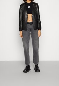 Blazer en cuir noir porté sur un haut court en maille noire, associé à un jean gris à jambes droites et des bottes noires à semelle épaisse. Design minimaliste.