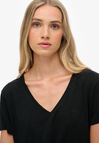 Zwart v-hals t-shirt gemaakt van lichtgewicht stof, met korte mouwen en een klein logo op de borst. Gladde textuur en eenvoudig ontwerp.