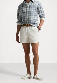 Sininen ja valkoinen ruudullinen paita, valkoiset shortsit, ruskea vyö ja valkoiset sneakersit. Paidassa on pitkät hihat, jotka on hieman kääritty ylös; shortsit ovat polvipituiset.