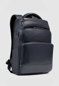 Mochila de cuero azul marino con múltiples compartimentos, cremalleras y una textura suave. Cuenta con correas acolchadas y un logo de la marca en el frente.