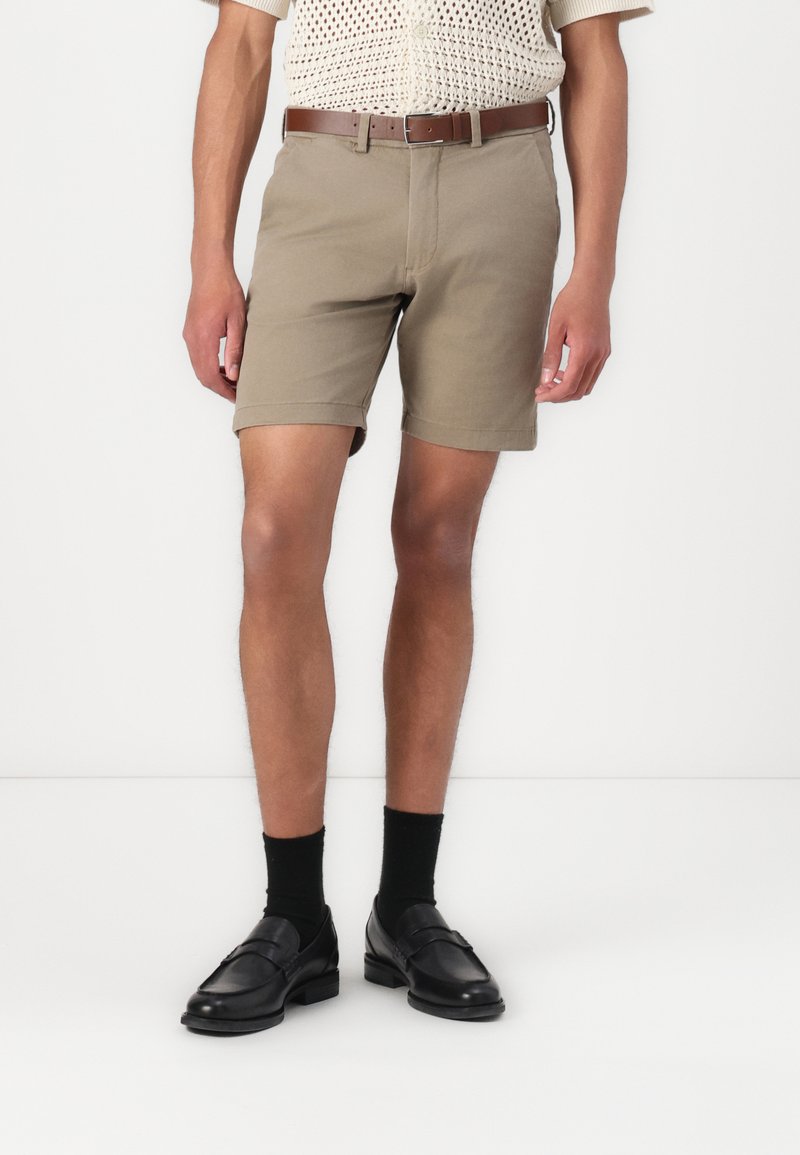 Beige bomulds shorts med oprullede kanter, båret med sorte strømper og loafers. Outfittet inkluderer en tekstureret, strikket top og et brunt bælte.
