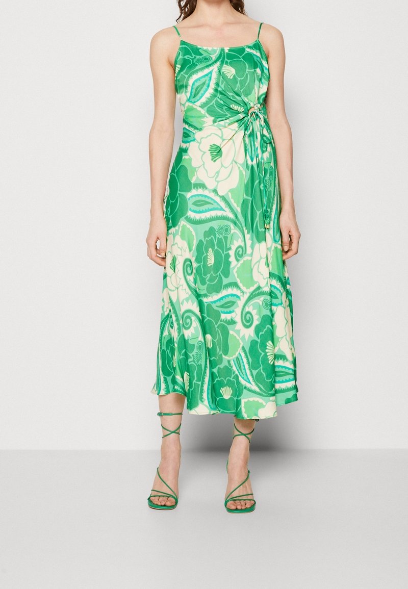 Grøn blomsterkjole med spaghetti-stropper, omslagsdesign og nederdel i mellem længde. Glat stof med store grønne og cremefarvede mønstre. Grønne sandaletter med stropper.