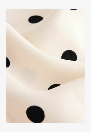 Kreemivärvi kangas, millel on suured mustad täpid, sile tekstuur, langevates voltides näidates materjali paindlikkust ja disaini.