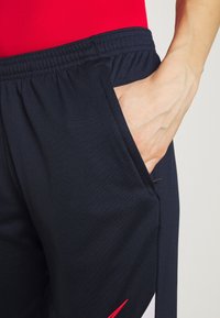 Marina atletiska shorts med en smidig textur, elastisk midja, sidficka och en röd accent på underbenet. Designade för komfort och rörelse.