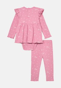 Rosa baby antrekk som inkluderer en langermet topp med volanger på skuldrene og en skjørtedesign, kombinert med matchende tettsittende bukser, alt dekorert med hvite hjerte mønstre og logo.
