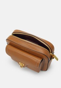 Ruskea nahkainen käsilaukku, jossa on kultainen vetoketju ja metalliosat. Laukussa on kaksiosainen muotoilu ja näkyvät ompeleet. Sisäpuoli on tummalla vuorella.