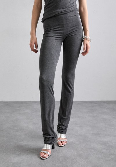Leggings gris ajustés en tissu doux et extensible, avec une taille mi-haute et des jambes effilées, associés à des sandales à talons hauts argentées.
