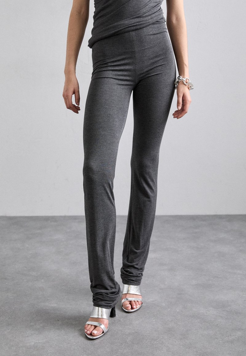 Leggings gris ajustés en tissu doux et extensible, avec une taille mi-haute et des jambes effilées, associés à des sandales à talons hauts argentées.