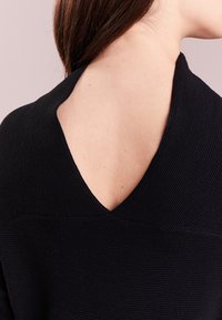 Top nero a coste con scollatura a V sul retro in tessuto testurizzato. Il design enfatizza un'estetica minimalista e un taglio distintivo.