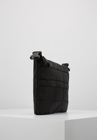 Borsa rettangolare nera caratterizzata da un design testurizzato e trapuntato con cuciture visibili. Dotata di doppie tracolle e chiusura con zip.