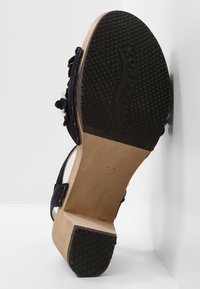 Sandalo con tacco alto in suede nero, caratterizzato da un tacco in legno, dettagli con cinturino regolabile e una suola in gomma testurizzata per una migliore aderenza.