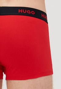 Boxer da uomo rossi in cotone, con un elastico nero che presenta il logo "HUGO" in rosso. Texture liscia e design aderente.