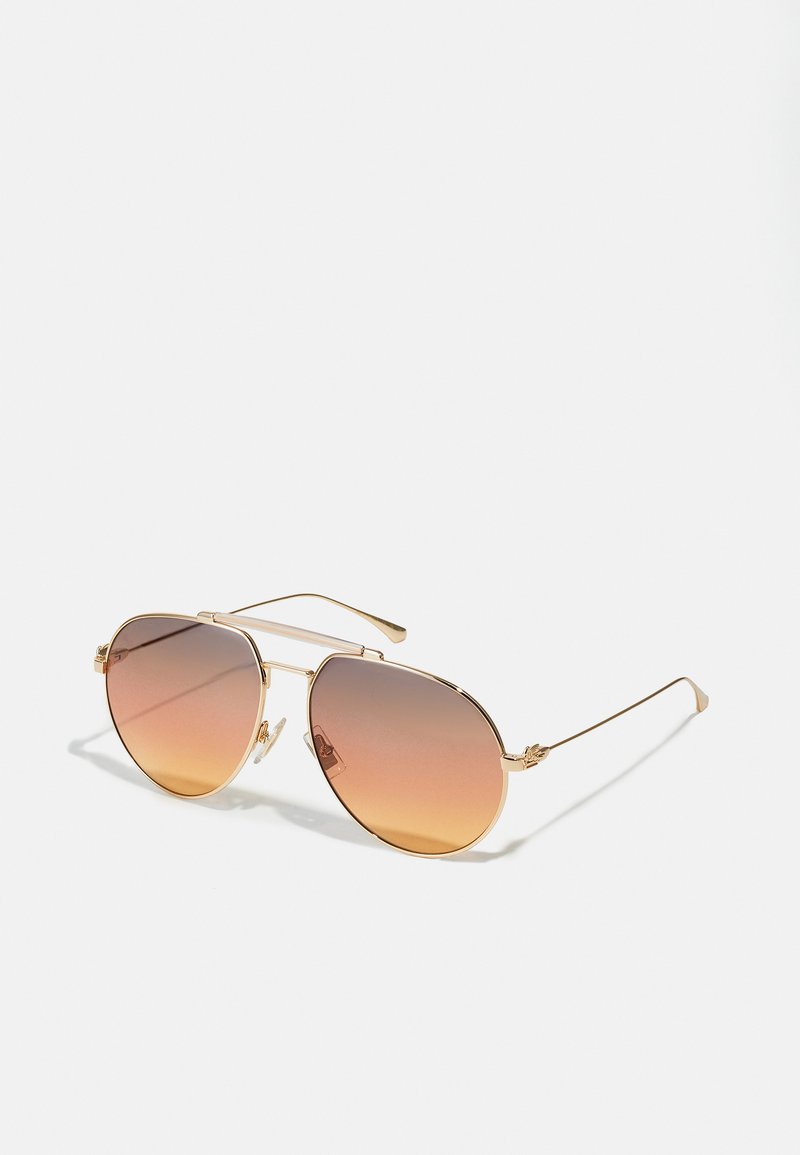 Ochelari de soare în stil aviator, cu rame subțiri din metal aurit și lentile nuanțate de la maro la portocaliu, pe un fundal alb.