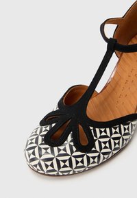 Παπούτσι με ασπρόμαυρο μοτίβο, στρογγυλεμένη μύτη, σχέδιο με κοψίματα, επάνω μέρος από σουέντ και δερμάτινη εσωτερική σόλα. Ορατή υφή στην εξωτερική σόλα.