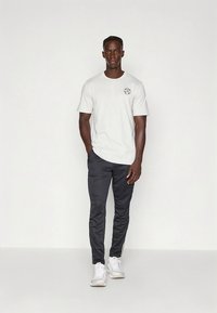 Balti medvilninė marškinėliai su grafiniu dizainu, derinami su juodomis sportinėmis kelnėmis, turinčiomis šonines juostas, ir baltais sportbačiais. Minimalistinis dizainas.