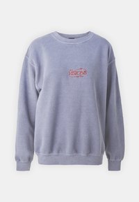 Ljusblå sweatshirt gjord av mjukt material, med rundad halsringning, ribbade ärmslut och en röd broderad logotyp på framsidan.