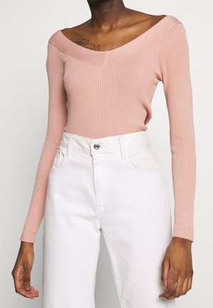 Gerippetes, schulterfreies Oberteil in sanftem Rosa, mit langen Ärmeln und V-Ausschnit, kombiniert mit hochgeschnittenen weißen Jeans. Die Textur ist glatt.