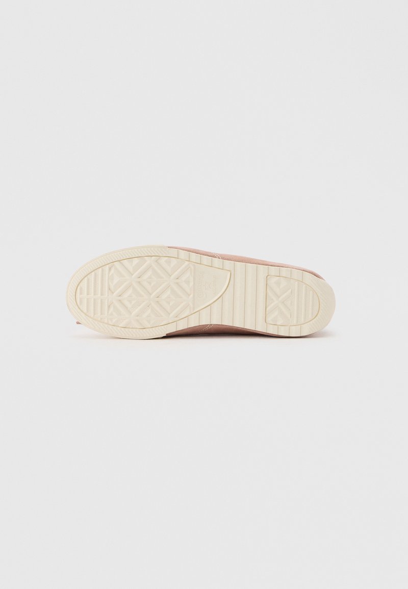 Sohle eines pinkfarbenen Sneakers mit beige gemusterter Gummisohle auf schlichtem hellgrauem Hintergrund.