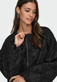 Črna bomberska jakna s cvetličnim vzorcem, z zadrgo in nabranimi rokavi. Ima lahkoten, vzorčen material in sproščen kroj.