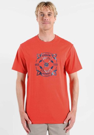 T-shirt en coton rouge avec un motif graphique bleu de feuilles et le texte « OXBOW » et « DEPUIS 1985 » disposés en cercle. Manches courtes.