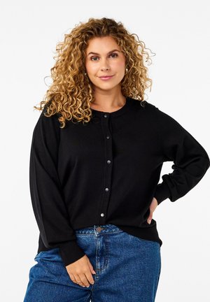 Cardigan noir à boutons en matériel tricoté doux, avec un col rond, des poignets côtelés et une coupe décontractée, associé à un jean en denim bleu.