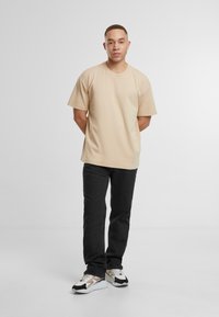 Tricou bej cu mânecă scurtă, cu o croială lejeră, asortat cu blugi negri din denim și adidași în tonuri neutre. Design simplist, detalii minime.