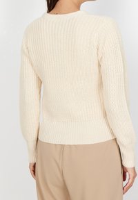 Krémový pletený svetr s ribbovanou strukturou, přiléhavými manžetami a lemem. Zadní část má střední délku a kulatý výstřih.