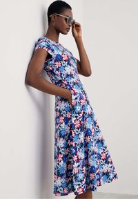 Floral dress in shades of blue with red and white accents, featuring a fitted bodice, cap sleeves, and side pockets. Smooth fabric with a flowing skirt.