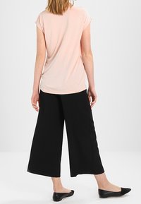 Haut rose clair à manches courtes associé à un pantalon noir à jambes larges, avec une texture lisse et un design simple. Des ballerines noires complètent l'ensemble.
