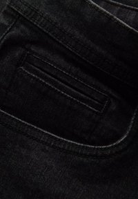 Tela de mezclilla negra con una vista en primer plano de un bolsillo trasero. Presenta una textura suave y costuras visibles a lo largo de los bordes.