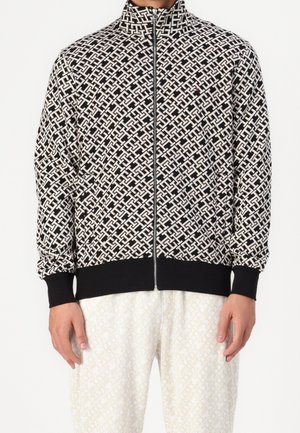 Černo-bílá vzorovaná bunda na zip s vysokým límcem a jednobarevnými černými lemy na rukávech a spodním okraji. Materiál je měkký s texturovaným povrchem.