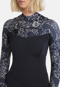 Wetsuit with navy floral pattern sleeves, black torso, high collar, and front zipper. Made of flexible material with reinforced stitching.
