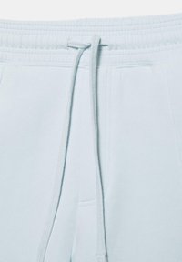Pantalon de survêtement bleu clair à taille avec bande élastique et cordons de serrage noués, montrant les poches avant et les détails de couture.