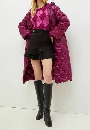 Manteau rembourré magenta avec un design matelassé, associé à un pull argyle violet et une jupe noire à volants, complété par des bottes noires montantes.