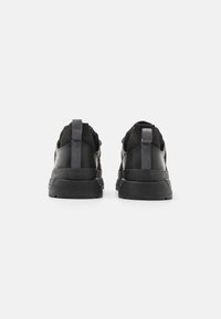 Paire de chaussures de sport noires avec semelles épaisses et languettes en tissu aux talons, vues de dos sur un fond blanc uni.