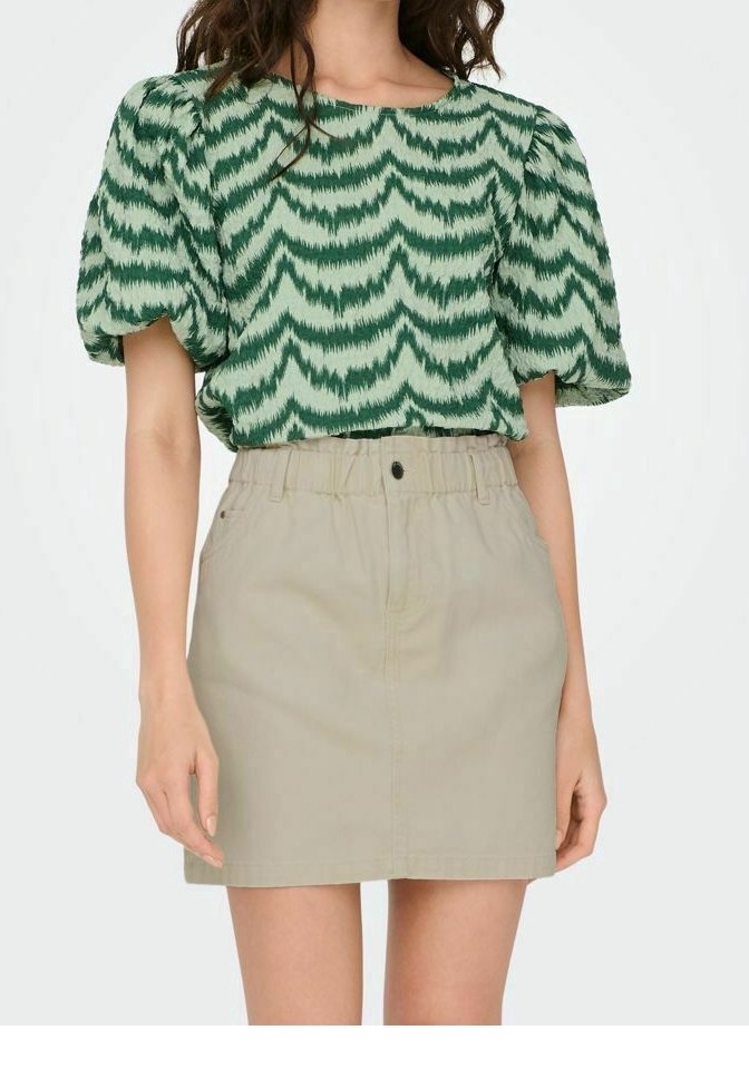 Haut à manches bouffantes à motif zigzag vert, associé à une mini-jupe beige avec une taille et une fermeture à boutons devant.