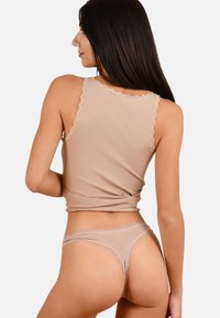 Beige Baumwoll-Top ohne Ärmel mit Spitzenbesatz am Ausschnitt und an den Armausschnitten, kombiniert mit passendem Spitzenbesatz-Tanga, der eine glatte Textur zeigt.