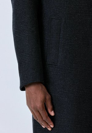 Dark plaid wool coat with a straight, structured design. Features a single side pocket and a tailored sleeve with a fold at the cuff.