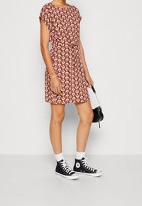 Short-sleeve A-line dress in a red and cream floral pattern, cinched at the waist, paired with black high-top sneakers and a small black handbag.