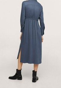 Vestito lungo blu con vita aderente e maniche lunghe, dotato di uno spacco laterale, abbinato a stivaletti neri alla caviglia. Tessuto morbido.