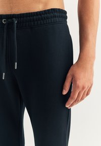 Zwarte joggingbroek met een elastische tailleband met trekkoord, zijzakken en een gladde, lichtgewicht stoftextuur.
