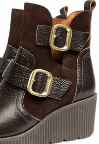 Botas de tobillo de cuero marrón y ante con doble hebilla, acabados texturizados y suela de plataforma estriada. Presentan un diseño en capas y contrastante.