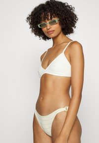 Top de bikini em triângulo branco com alças ajustáveis, acompanhado de um fundo de corte baixo combinando, com riscas horizontais e um detalhe de fivela lateral.