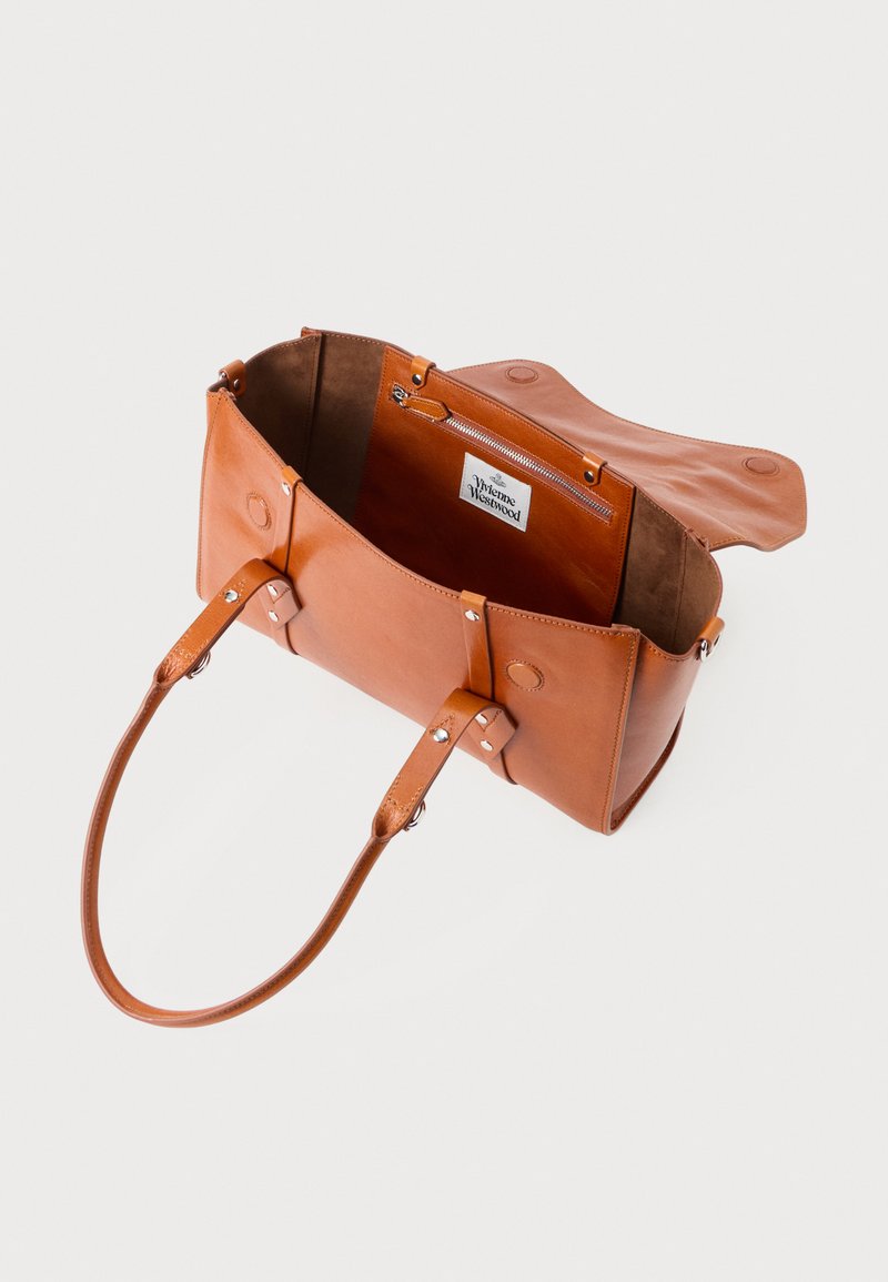 Sac fourre-tout en cuir brun avec deux poignées, ouverture sur le dessus et poche zippée intérieure ; présente une texture lisse et des détails de coutures visibles.