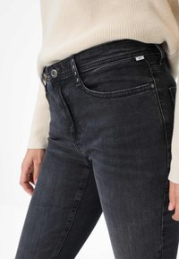 Jeans in denim nero con una vestibilità slim, design a cinque tasche e dettagli in metallo sulla parte anteriore. Texture liscia con leggere sfumature.