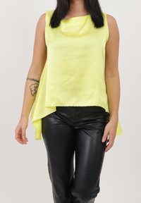 Geel mouwloos topje van een lichtgewicht stof met een asymmetrische zoom, gecombineerd met zwarte leren broek met een ontspannen pasvorm.