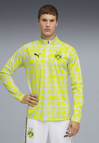 Långärmad sportpullover i ljusgrått med djärva neongula geometriska mönster, med en halvdragkedja i kragen och Puma-logotyp.