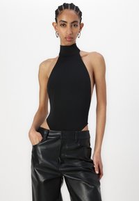 Czarny bodysuit na halter z wysokim dekoltem i wycięciami po bokach, wykonany z elastycznego materiału. W połączeniu z czarnymi, skórzanymi spodniami o wysokim stanie.